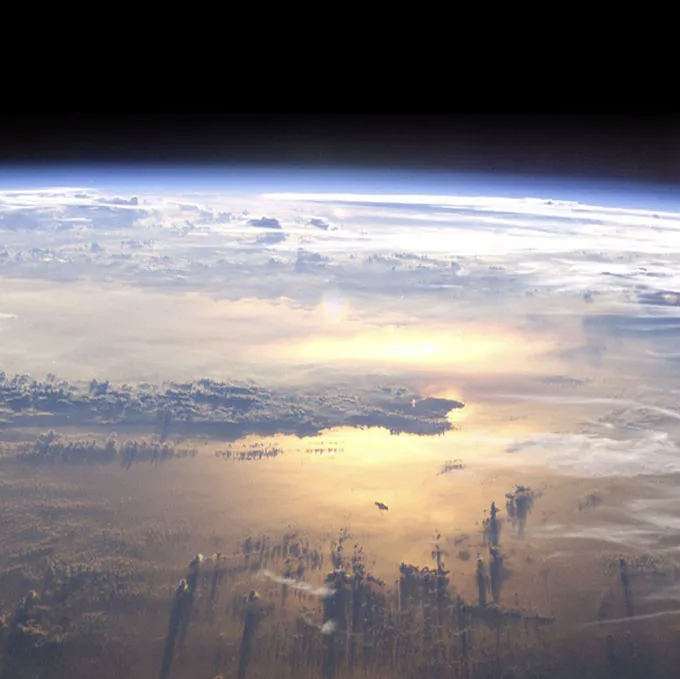 Die Erde ist im Anschnitt zu sehen. Wolken und eine sich reflektierende Sonne