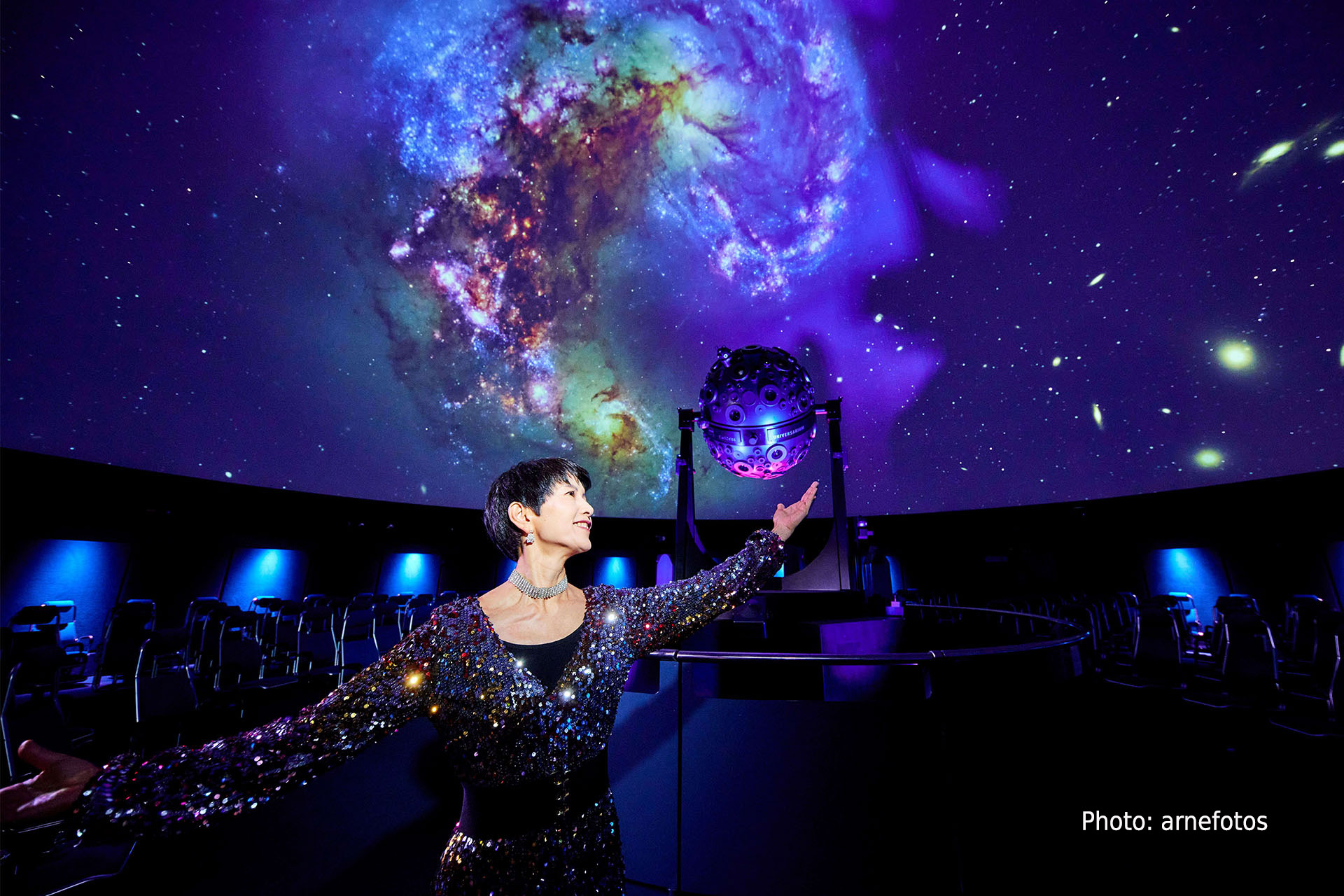 Eine Frau steht in einer Balletpose in der Kuppel, vor Sternenhimmel und dem Universarium