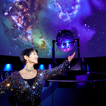 Eine Frau steht in einer Balletpose in der Kuppel, vor Sternenhimmel und dem Universarium