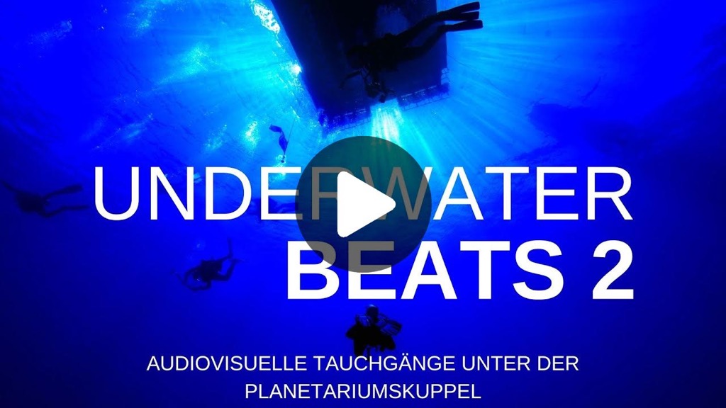 Ein Tauchboot ist von unten aus der Tiefe gegen das Sonnenlicht fotografiert. Alles in einem tiefen Blau. Taucher sind in der Silhouette zu erkennen. Ein PLAY-Button liegt auf dem Bild. Text: UnderwaterBeats2. Audiovisuelle Tauchgänge unter der Planetariumskuppel.